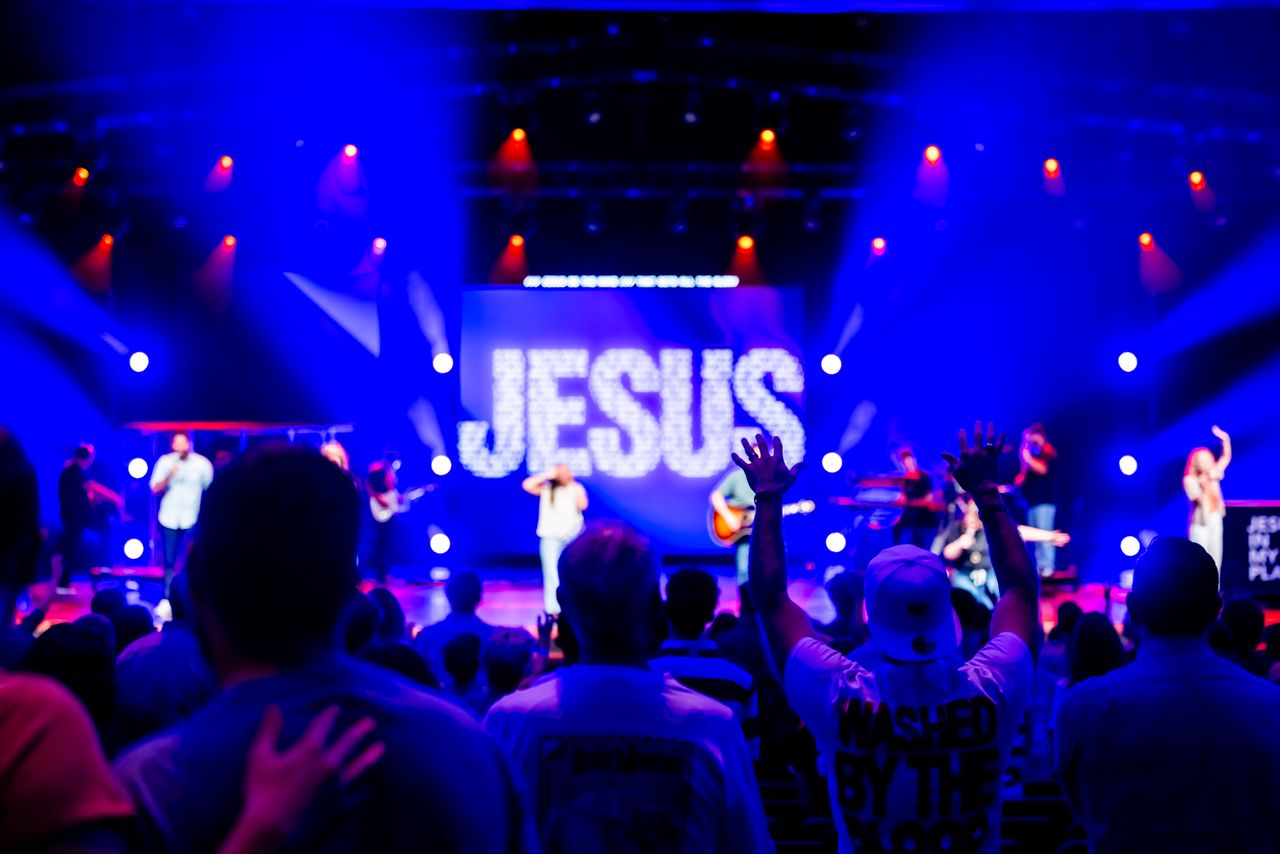 Lively religious concert with a band and audience worshipping under colorful stage lights.